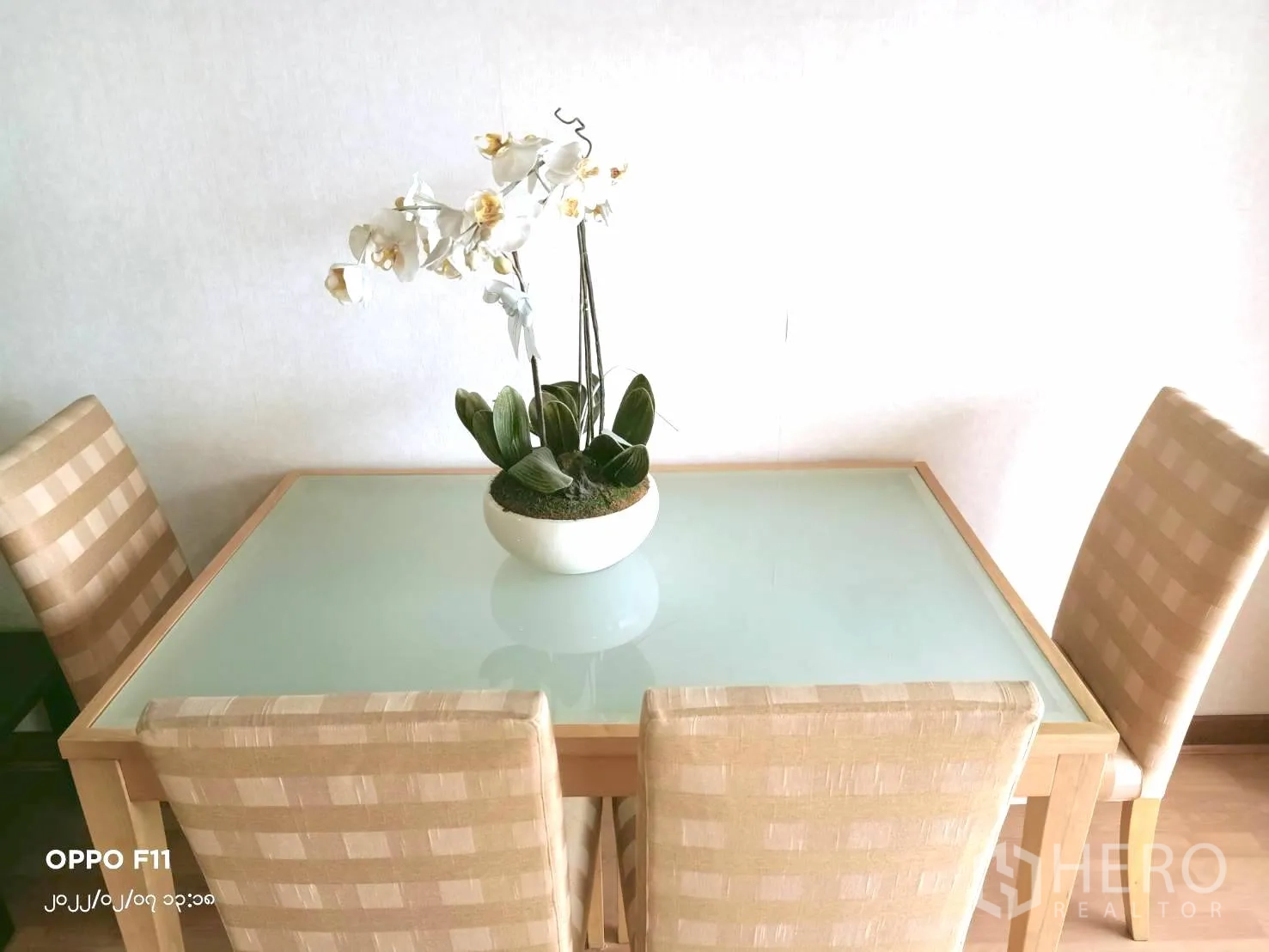 Condominium for rent in Khlong Toei, Bangkok - Close-up of a glass-top dining table with four upholstered chairs and a potted orchid.