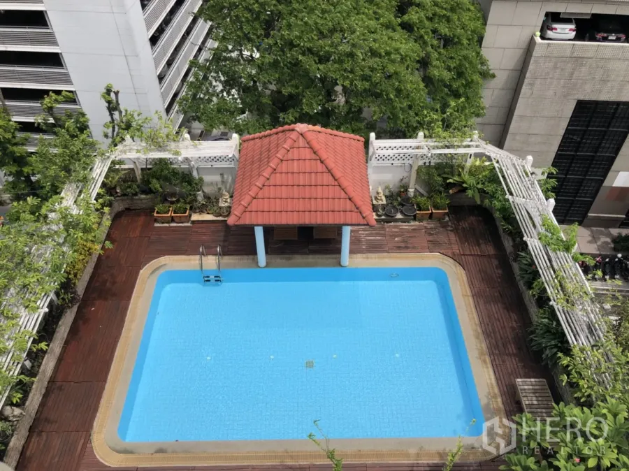 Apartment for rent in Bang Rak, Bangkok - Rooftop outdoor swimming pool with red-tile pavilion and wooden deck surrounded by city greenery.