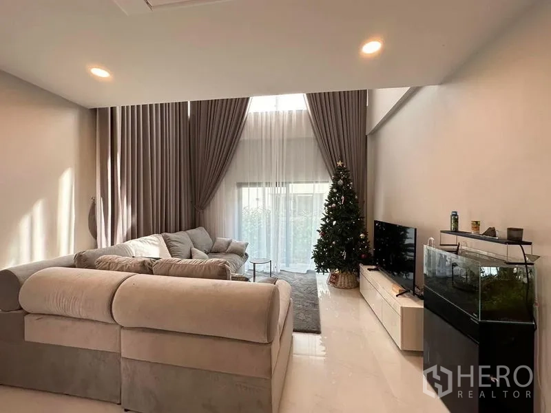 Detached House for rent in Bang Phli, Samut Prakan - Open-plan lounge with high windows, TV unit, aquarium and sliding glass doors to the garden.