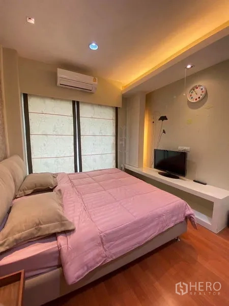 公寓 出租或出售在Bang Kapi, Bangkok - 卧室配粉色床品、空调与小型电视台，灯光柔和。