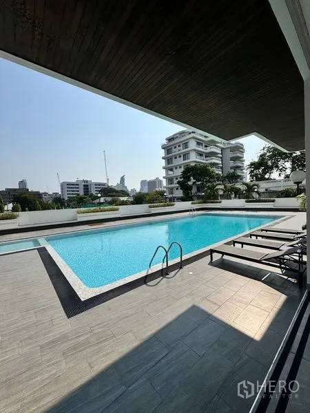 房间 出租在Khlong Toei, Bangkok - 大型室外游泳池与躺椅，周围是城市建筑景观。