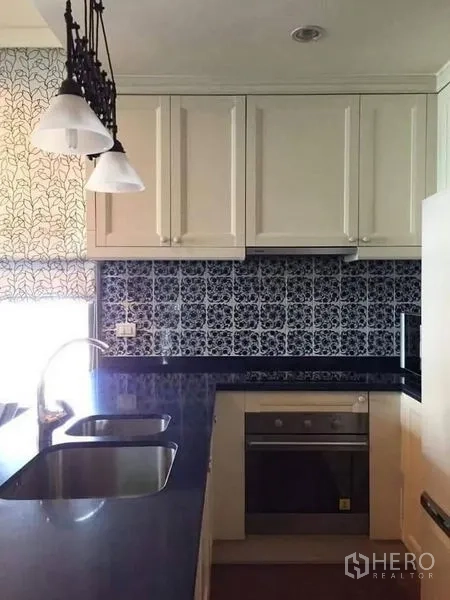 Condominium for rent in Khlong Toei, Bangkok - Fitted kitchen with stone countertops, sink, built-in oven and pendant lights over the counter.
