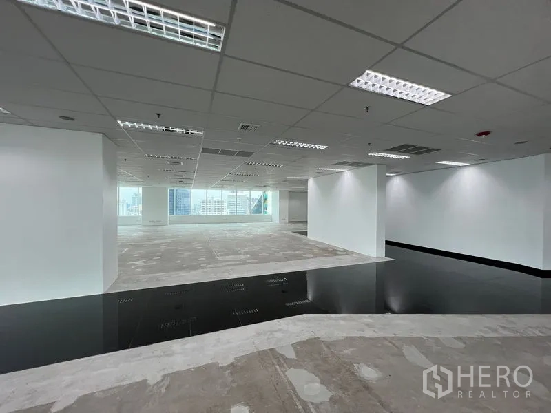 สำนักงาน ให้เช่า - โซนทำงานโล่ง ผนังสีขาว พื้นยกบางส่วน และหน้าต่างเต็มผนังมองเห็นวิวเมือง