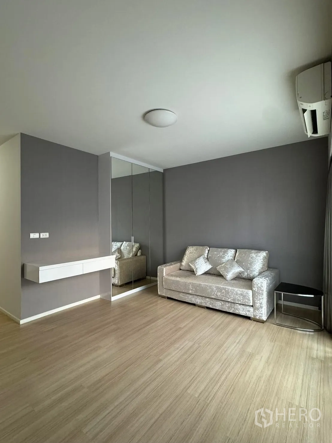 Townhouse for rent in Suan Luang, Bangkok - Minimalist sitting area with silver sofa, mirrored wardrobe and light wood flooring.