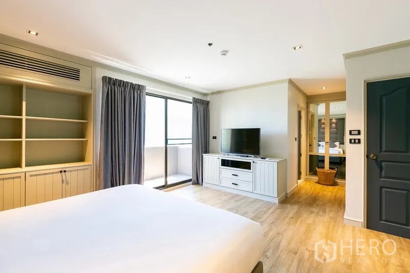 Apartment for rent in Khlong Toei, Bangkok - Master bedroom view showing TV console, sliding balcony door, and light wood flooring.