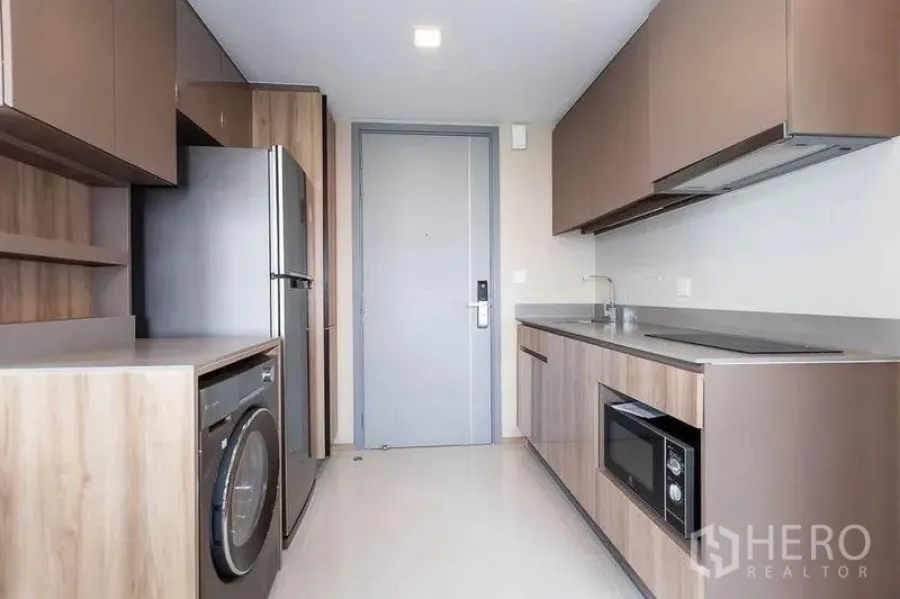 公寓 出租在Watthana, Bangkok - 走廊式现代厨房，木质橱柜，配冰箱、洗衣机、水槽与嵌入式灶台和微波炉