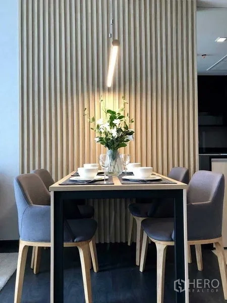 公寓 出租在Watthana, Bangkok - 四人餐桌摆放花瓶与餐具，暖色吊灯照明，背靠竖向木饰面。