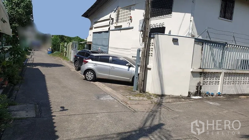 Warehouse for rent in Suan Luang, Bangkok - Narrow lane with cars parked beside a gated warehouse exterior in Suan Luang.