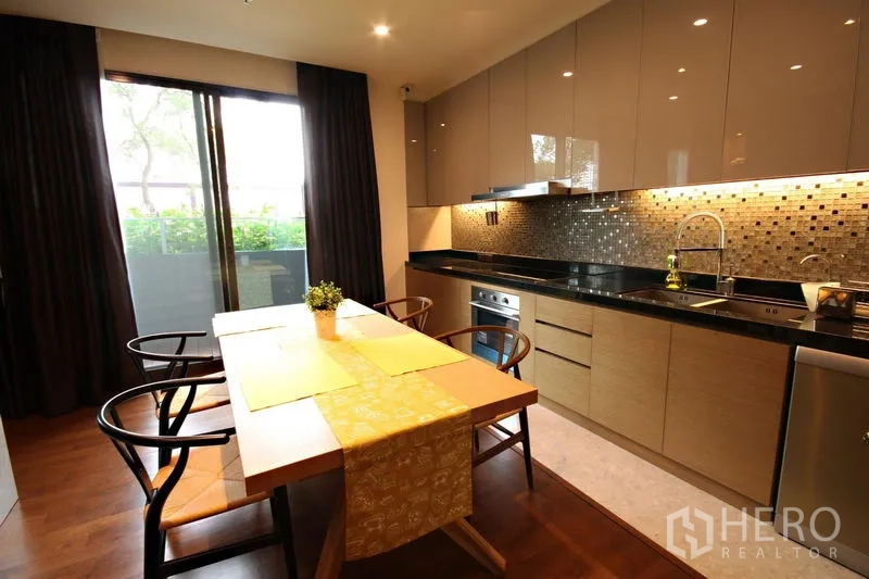 Condominium for rent or sale in Khlong Toei, Bangkok - Dining table beside balcony doors and a linear kitchen with glossy cabinets.