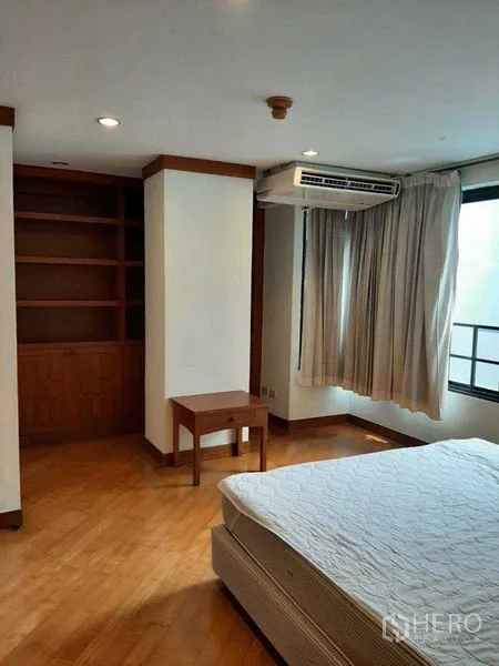 Apartment for rent in Watthana, Bangkok - Primary bedroom with large window, built-in shelving and air conditioning.