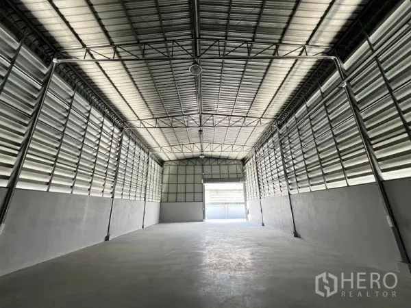 Warehouse for rent in Prawet, Bangkok - Spacious warehouse interior with high steel truss roof, louvered ventilation walls and open bay door.