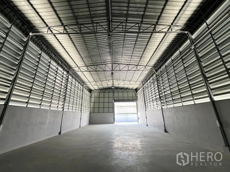 Warehouse for rent in Prawet, Bangkok - Spacious warehouse interior with high steel truss roof, louvered ventilation walls and open bay door.