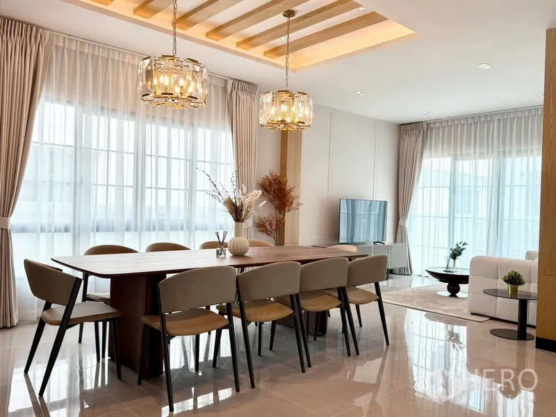 Detached House for rent or sale in Bang Phli, Samut Prakan - Dining area flowing to living room with pendant lights, TV wall and full-height glazing.
