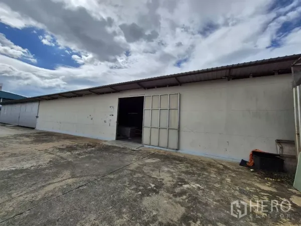 Warehouse for rent in Mueang Pathum Thani, Pathum Thani - Front view of ground-level warehouse facade with an open manual folding door and ample paved forecourt.