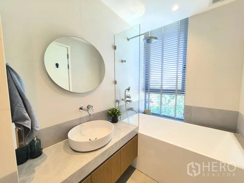 Apartment for rent - Bathroom with soaking tub, glass shower screen and round mirror beside a window.