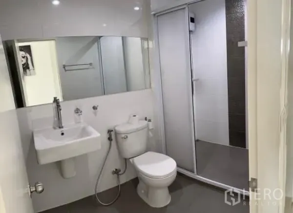 Condominium for sale in Khlong Toei, Bangkok - Bright bathroom with wall mirror, sink, toilet and enclosed shower.