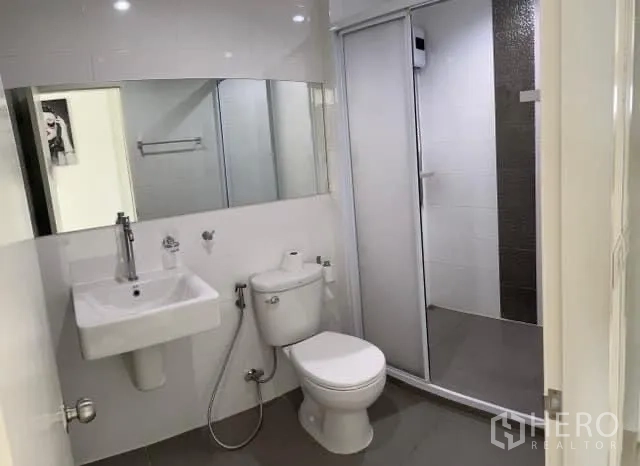 Condominium for sale in Khlong Toei, Bangkok - Bright bathroom with wall mirror, sink, toilet and enclosed shower.