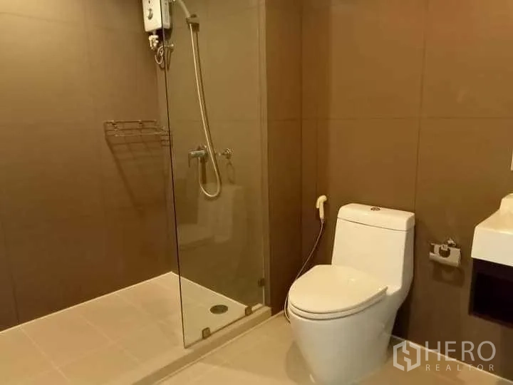 公寓 出租在Watthana, Bangkok - 现代浴室，玻璃淋浴间、热水器与白色马桶。