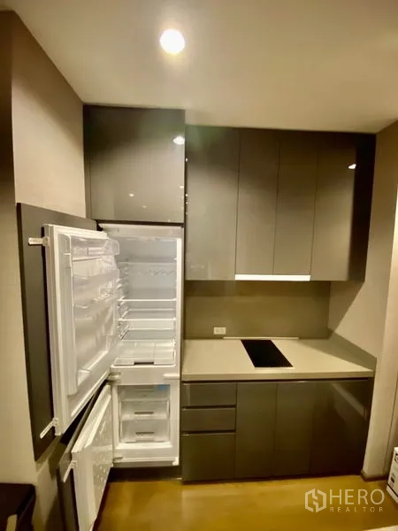 公寓 出租或出售在Bang Rak, Bangkok - 现代紧凑厨房，亮面橱柜、感应炉灶与打开的冰箱。