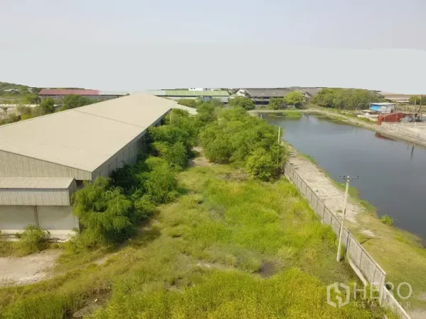 Factory for sale in Samut Prakan - Aerial of the factory sitting beside a canal with a concrete fence and open, overgrown land.