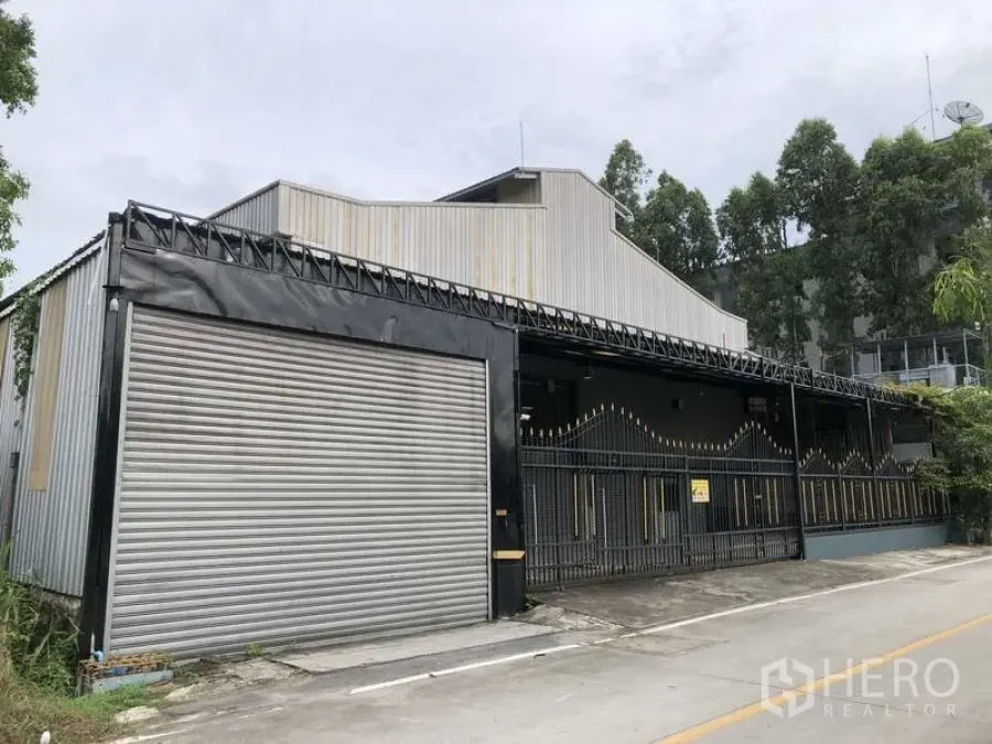 货栈 出租在Bang Phli, Samut Prakan - 临街仓库外观，带大型卷帘门与安全围栏入口。