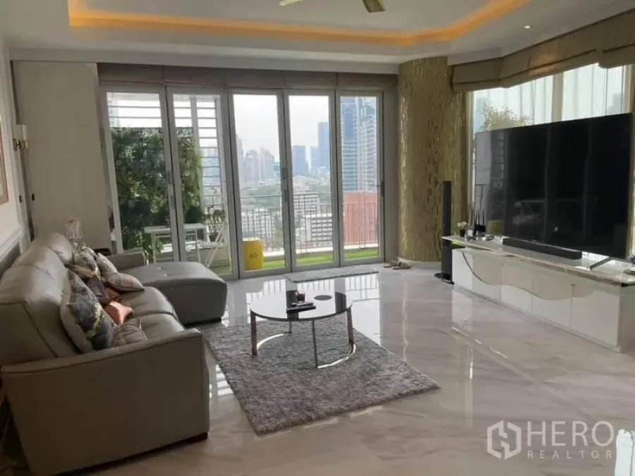 公寓 出售在Pathum Wan, Bangkok - 采光充足的客厅，石材地面，转角沙发，落地窗通向观景阳台与城市天际线。