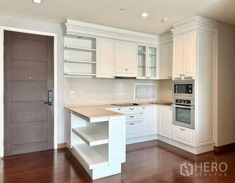 Condominium for rent in Watthana, Bangkok - White L-shaped kitchen with built-in oven, open shelving, and island counter.