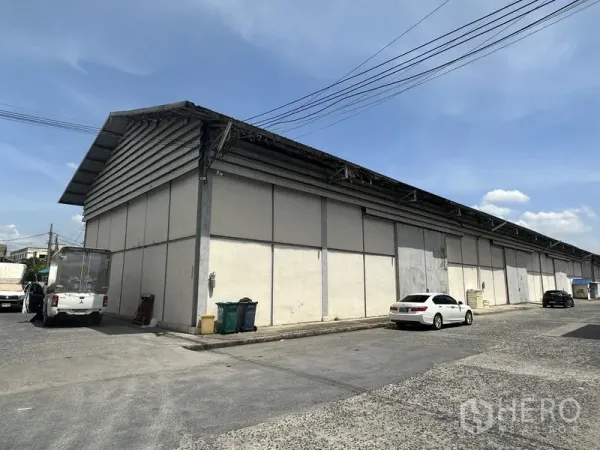 Warehouse for rent in Phra Nakhon Si Ayutthaya - Corner view of a large single-storey warehouse with metal roof and loading access on a wide service road.