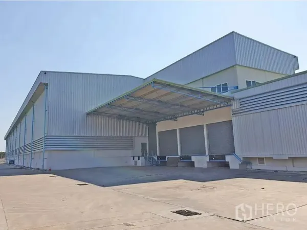 Warehouse for rent in Lat Krabang, Bangkok - Facade view showing multiple roller shutter loading docks under a canopy and ample yard space for truck maneuvering.