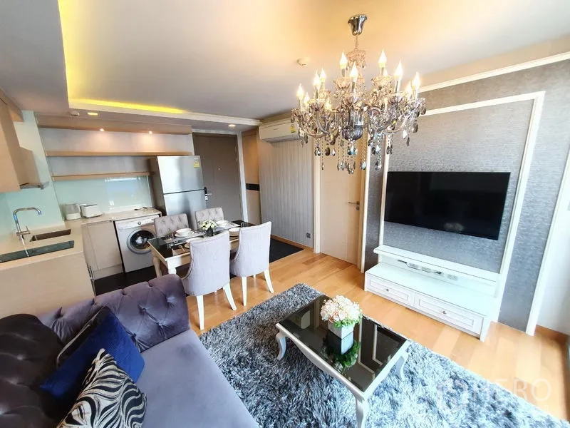 Condominium for rent in Watthana, Bangkok - Open-plan living room with chandelier, wall-mounted TV and compact kitchen in a Bangkok Watthana condominium.