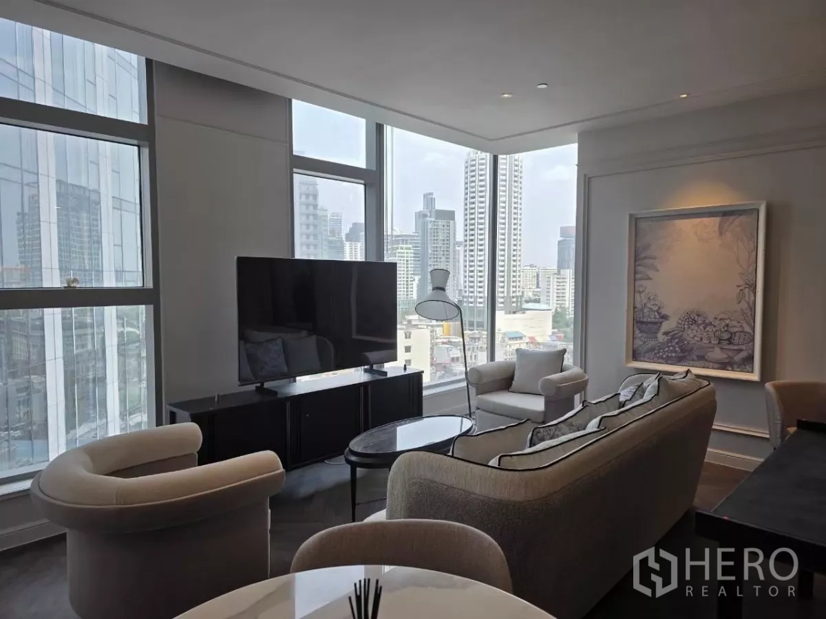Condominium for rent - Corner living room with TV console, curved armchairs, and skyline views through large windows.