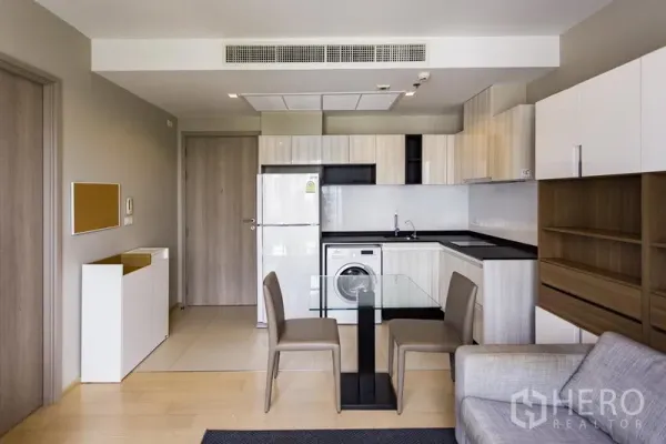 Condominium for rent in Watthana, Bangkok - Modern kitchen with built‑in cabinets, appliances and a glass dining set.