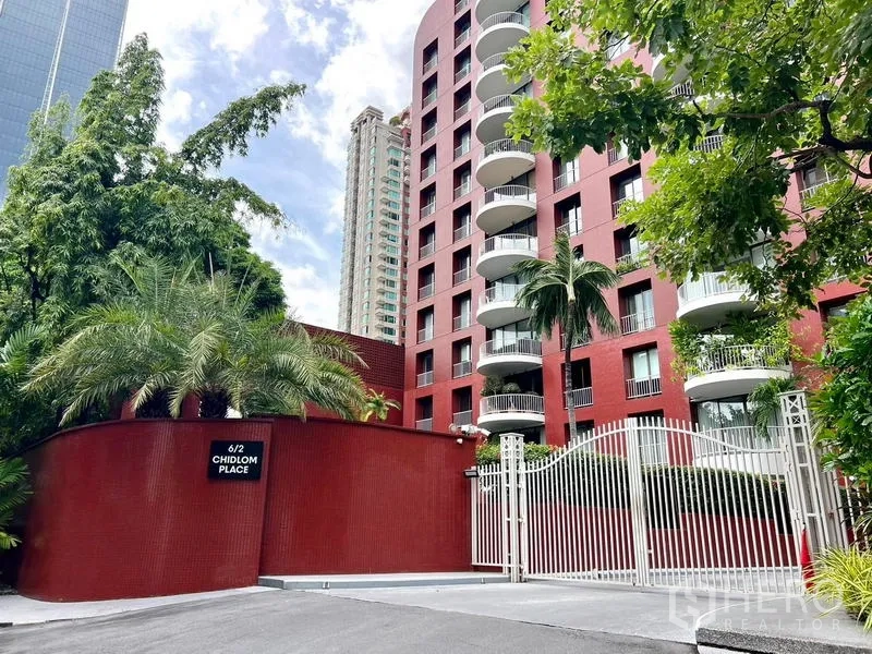 公寓 出售在Pathum Wan, Bangkok - 巴吞旺区红色外墙公寓楼，弧形阳台与门禁入口，绿树环绕