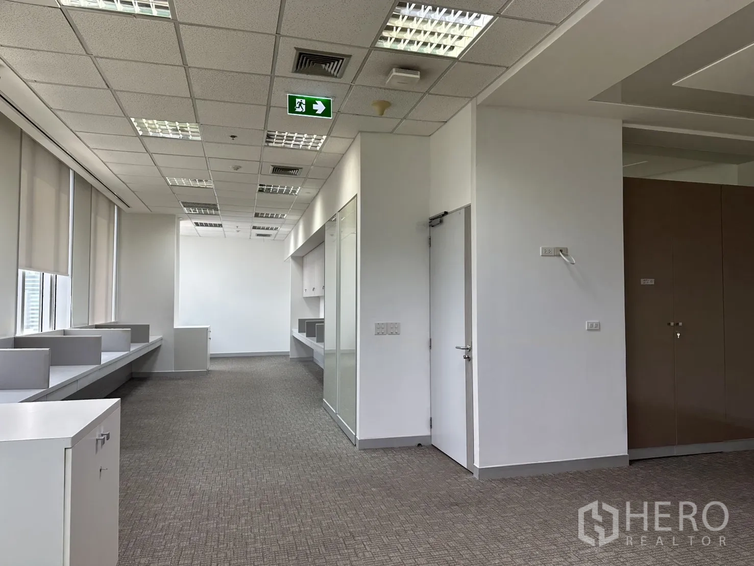 办公室 for rent in Khlong Toei, Bangkok - 狭长办公区，T 型格栅天花照明与紧急出口标识清晰可见。