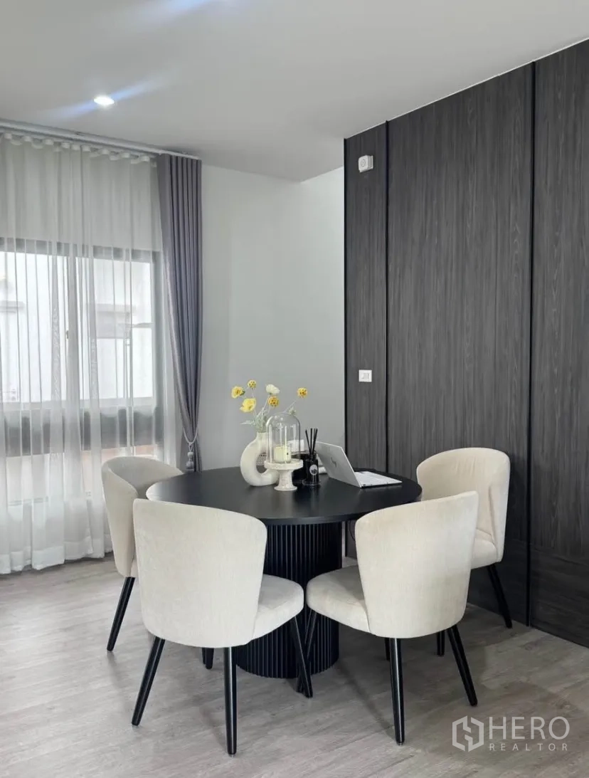 Detached House for rent or sale in Lat Krabang, Bangkok - Dining corner with round black table, four cream chairs, and sheer-draped window providing soft natural light.