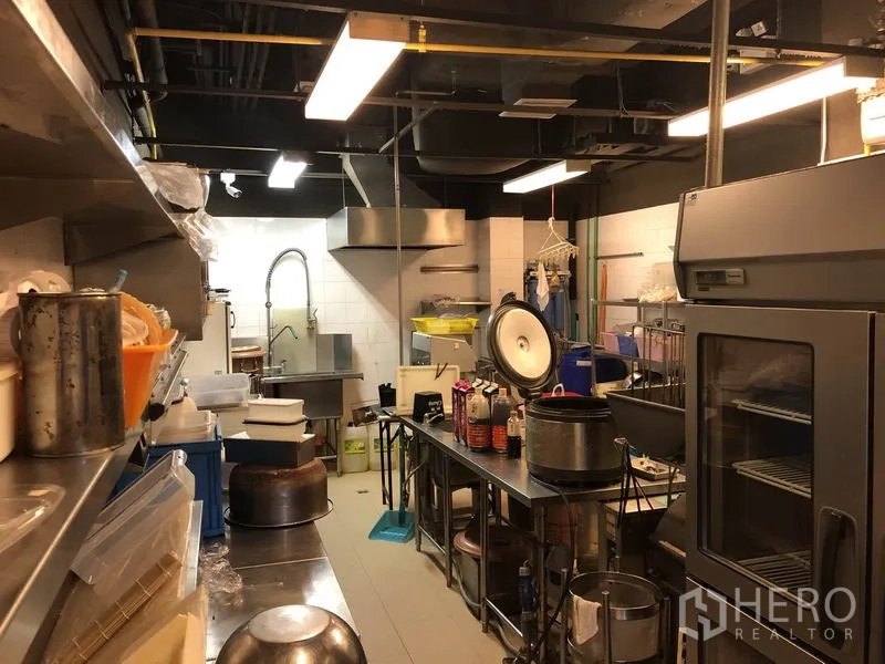 Retail Space for rent in Khlong Toei, Bangkok - Back-of-house kitchen with ventilation hoods, industrial sink, shelving and large refrigerator.