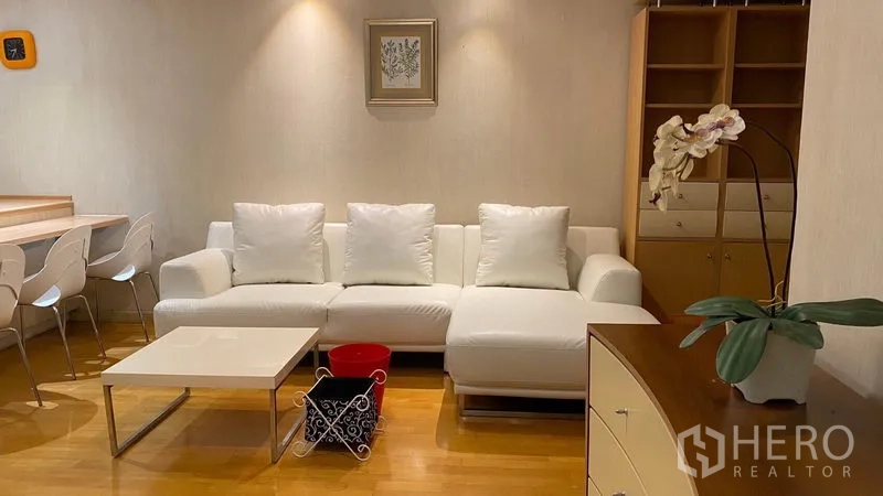 公寓 出租在Khlong Toei, Bangkok - 采光充足的客厅，L 形白色沙发、嵌入式置物架与简约茶几。