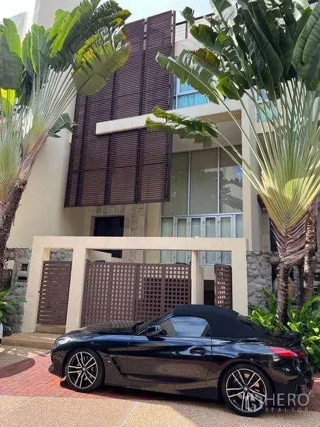 Townhouse for sale in Yan Nawa, Bangkok - Street-level view of gated townhouse framed by tropical landscaping and wooden screen accents.