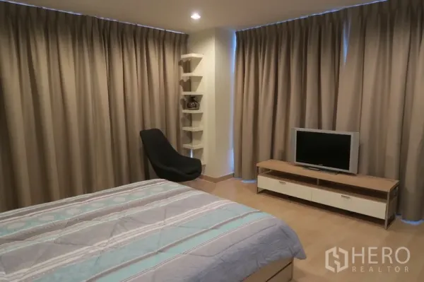 คอนโด ให้เช่าในHuai Khwang, Bangkok - ห้องนอนหลักกว้างพร้อมชั้นวางทีวี ชั้นวางมุม เก้าอี้นั่งพัก และผ้าม่านเต็มความสูง
