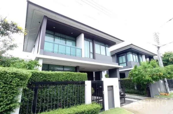 独立式住宅 出租在Bang Kapi, Bangkok - 斜角外观展示玻璃阳台、大面积落地窗与整齐绿篱。