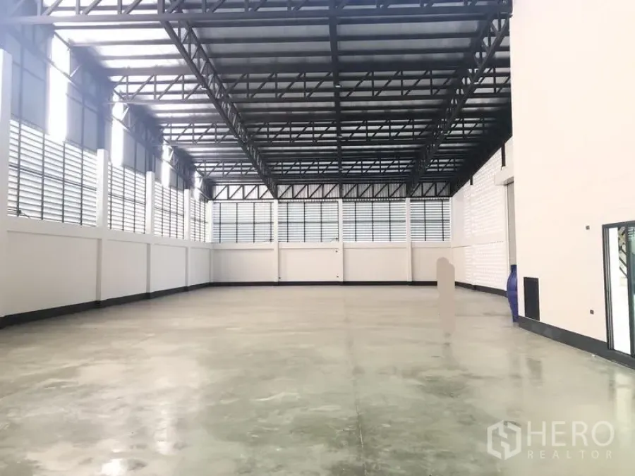 工厂 出售在Pathum Thani - 宽敞仓库内部，高钢桁架屋顶、抛光混凝土地面与百叶窗通风。