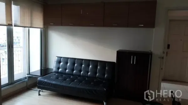 公寓 出租在Bang Rak, Bangkok - 客厅配黑色皮沙发、顶柜与带百叶的阳台窗。
