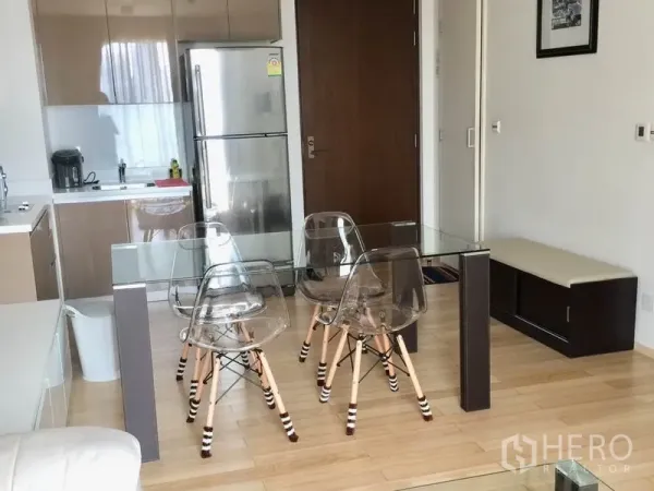 Condominium for rent in Khlong Toei, Bangkok - Compact kitchen with stainless refrigerator and a glass dining table with clear chairs.