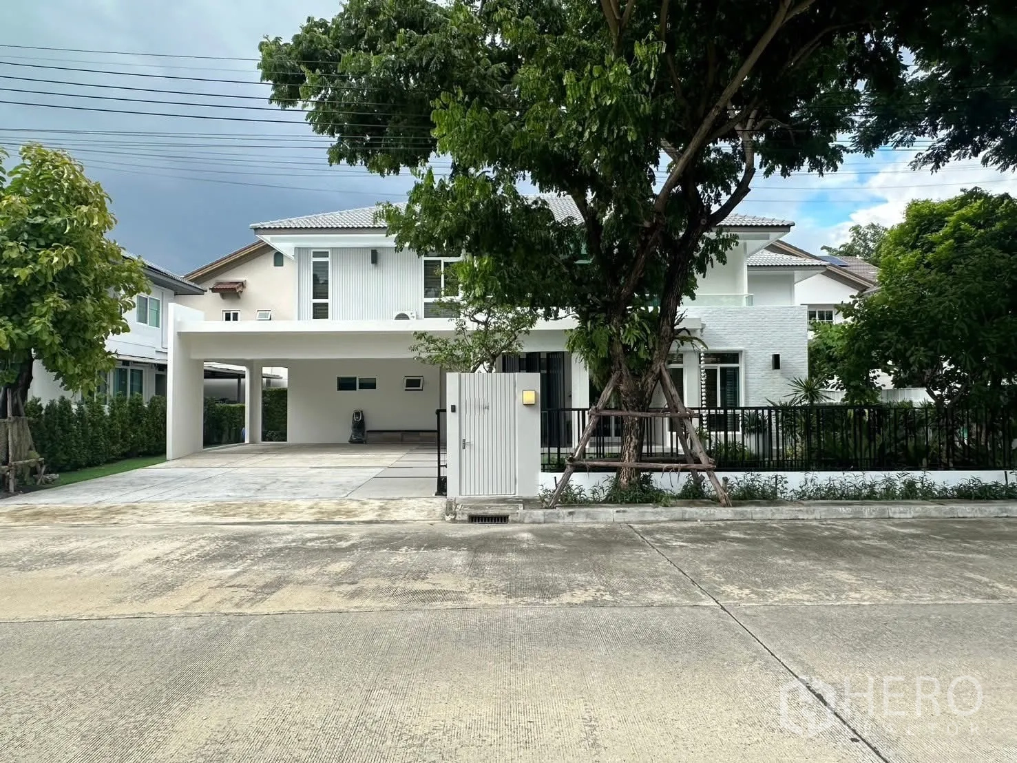 บ้านเดี่ยว for rent in Bang Phli, Samut Prakan - บ้านเดี่ยวสองชั้นโทนสีขาวพร้อมประตูรั้ว ถนนหน้าบ้านกว้างและมีต้นไม้ใหญ่.