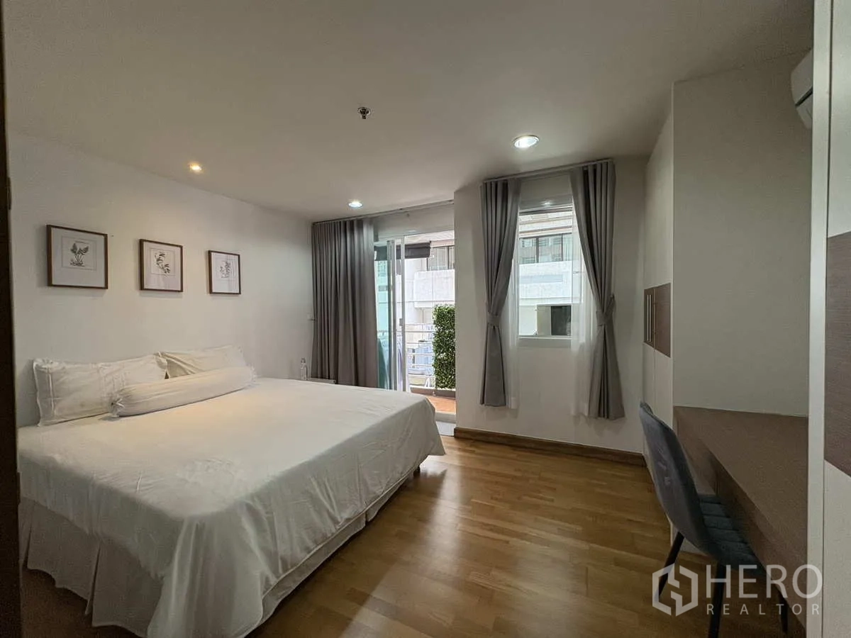 Condominium for rent in Khlong Toei, Bangkok - Bedroom with king bed, desk, windows and balcony access with curtains.