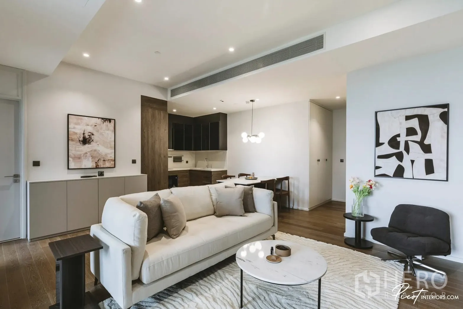 คอนโด for rent in Pathum Wan, Bangkok - ห้องนั่งเล่นกว้างพร้อมโซฟา โต๊ะกลางกลม งานศิลปะ และโซนครัว-รับประทานอาหารด้านหลัง