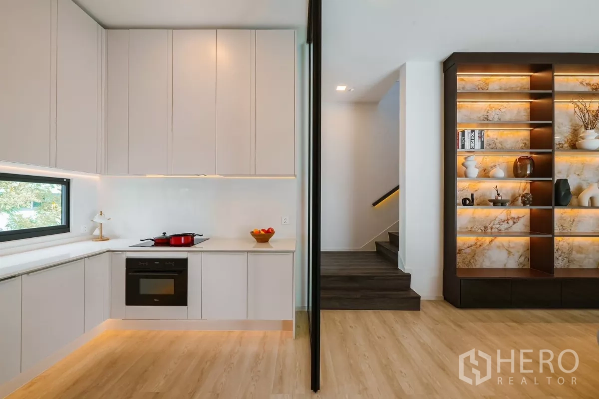 Detached House for rent or sale in Saphan Sung, Bangkok - Light L-shaped kitchen with built-in oven, window and display shelving by staircase.