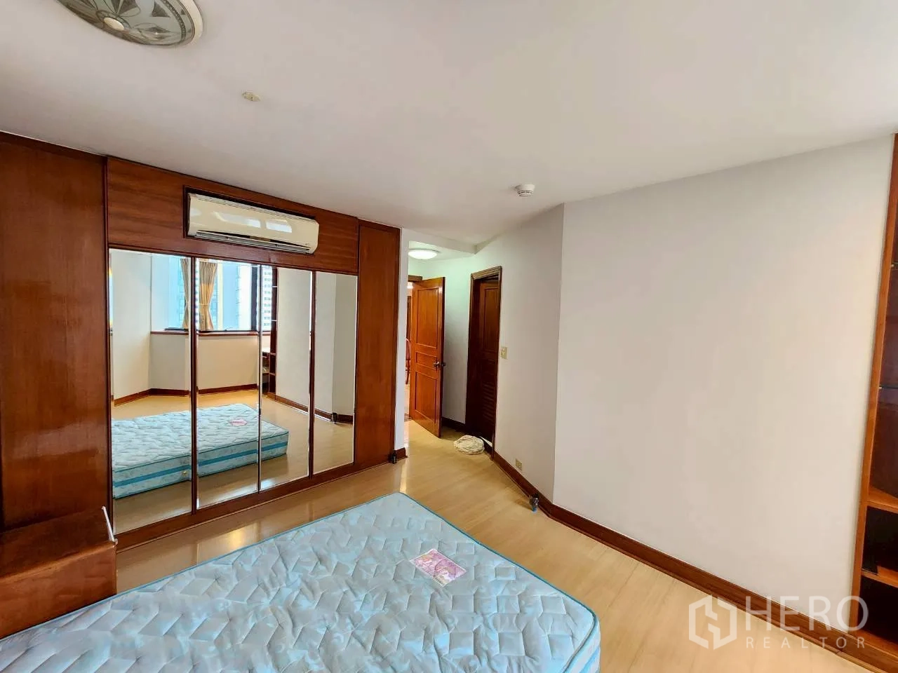 Condominium for rent in Khlong Toei, Bangkok - Second bedroom with mirrored wardrobe, air-conditioning unit and wood floors.