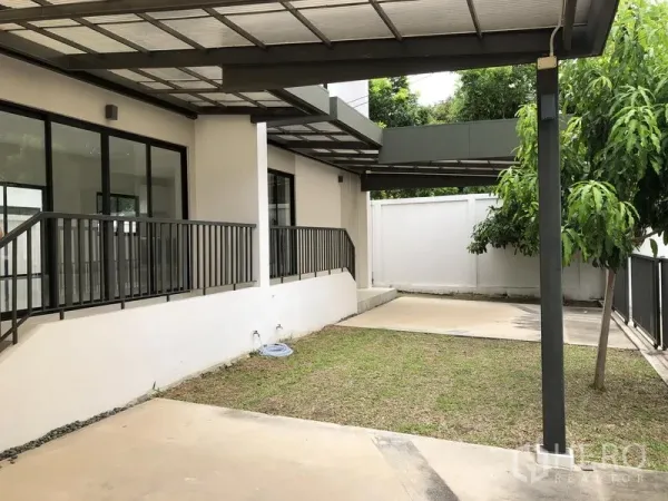Townhouse for rent or sale in Saphan Sung, Bangkok - Covered carport and small front lawn beside sliding glass doors and privacy wall.