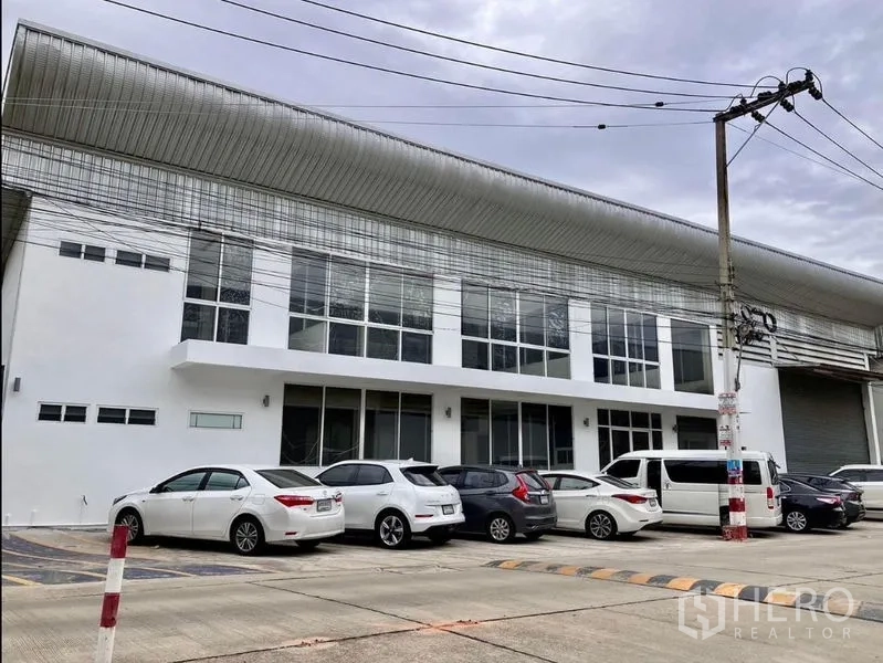 货栈 出租在Prawet, Bangkok - 现代白色仓库立面，整排落地玻璃，前方停车位与卷闸出入口。